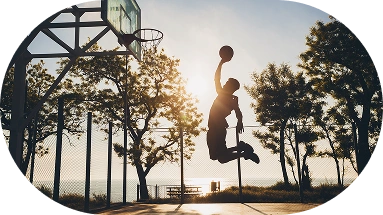 Silhouette of a basketball player performing a jump shot on an outdoor court during sunset with dramatic natural lighting.