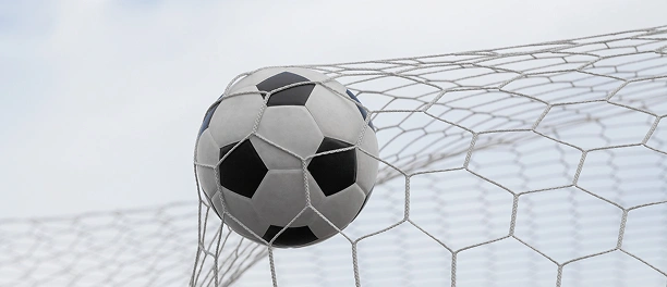 Close-up of a soccer ball hitting the goal net against a clean sky background during a football match.